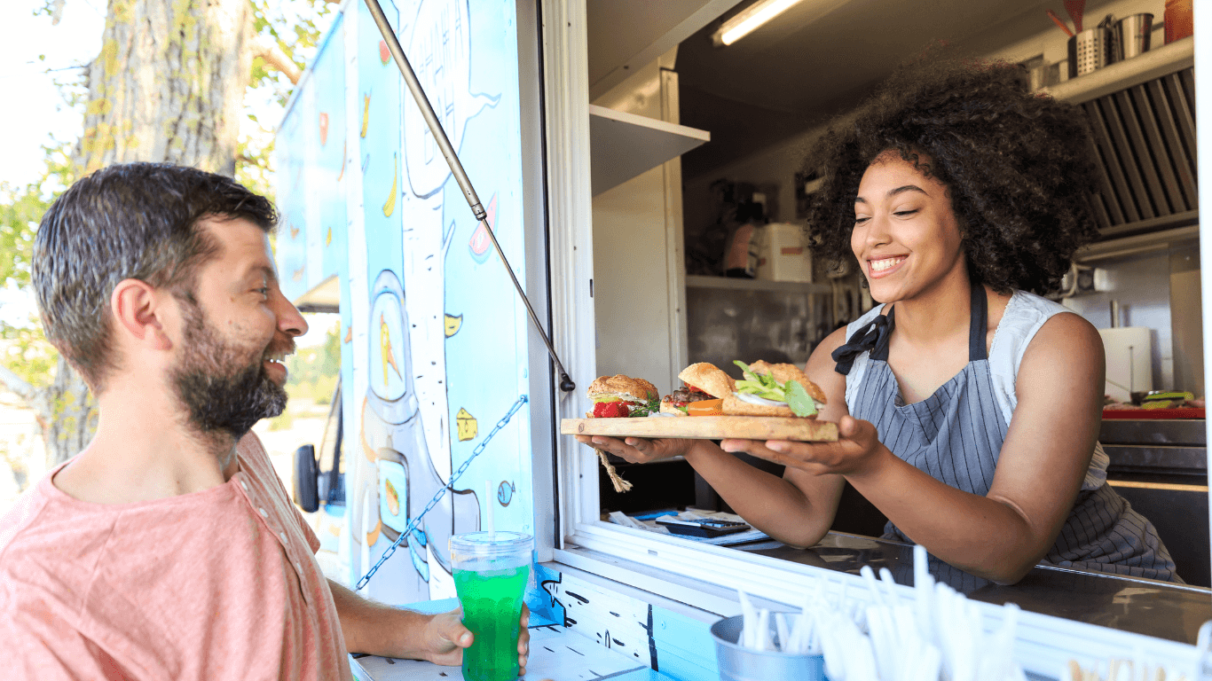 OpenAccesshero (1) Smiling woman serving a variety of sandwiches to a man from a food truck window