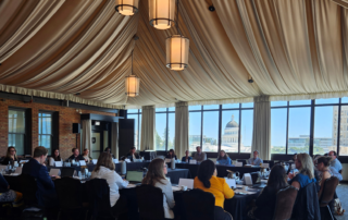 Convening room of people seated at an open rectangle table. In the background is the California State Capital building.